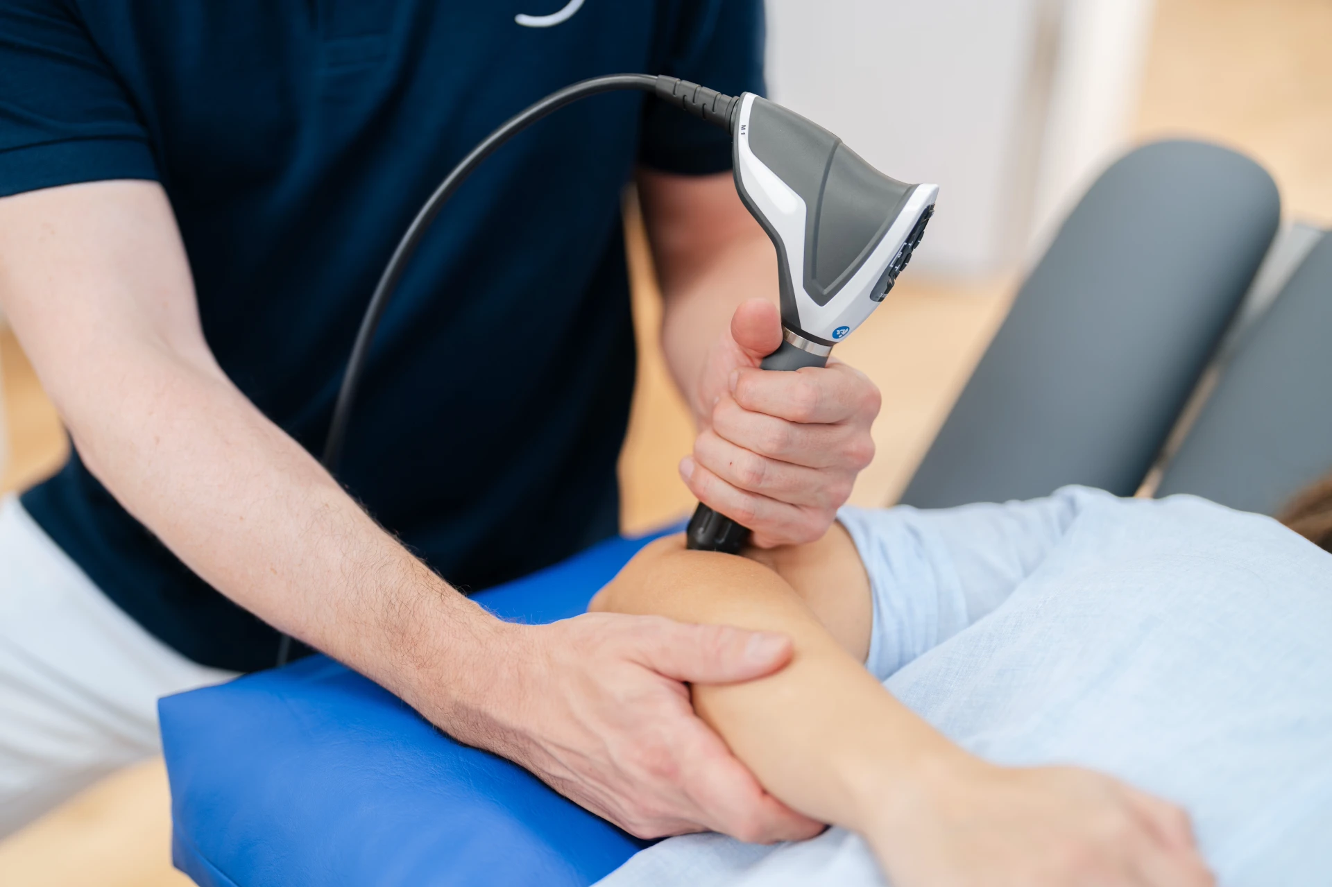Ein Therapeut behandelt den Arm einer Patientin mit einem medizinischen Gerät in einer Behandlungsumgebung.