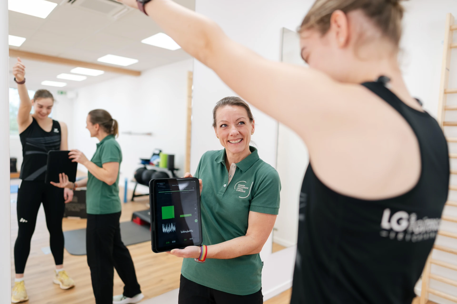 Eine Trainerin zeigt einer Sportlerin am Tablet eine Übungsauswertung in einem modernen Fitnessraum.